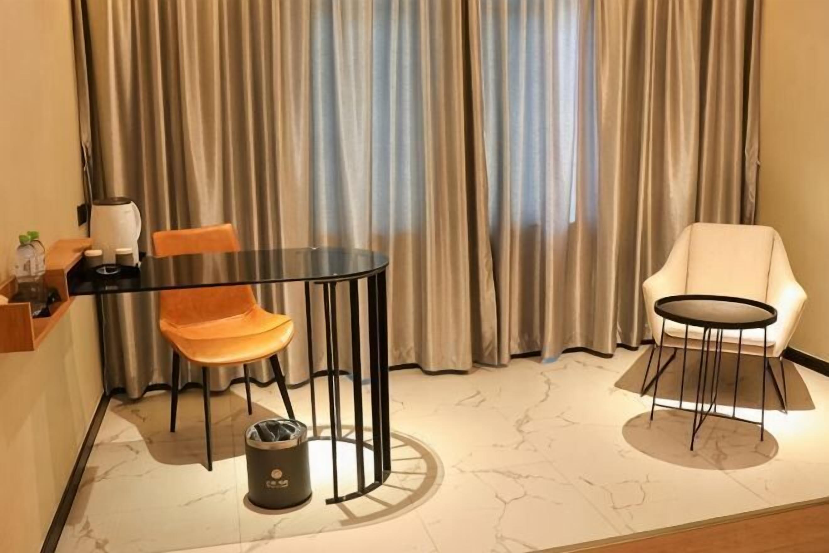 Een kamer met een ronde tafel, twee stoelen, een prullenbak en een raam met gordijnen.