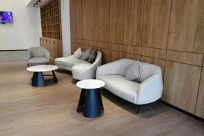 A modern lounge area with a sofa, two round tables, and a television screen. - Yicheng Hotel (Maoming China First Beach) (Maoming)