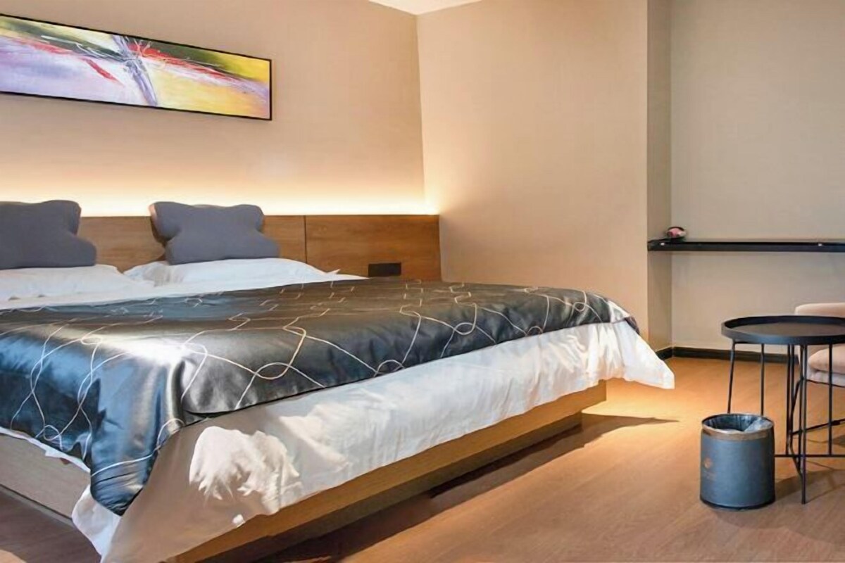 A modern hotel room with a large bed, a small round table, and a trash bin.
