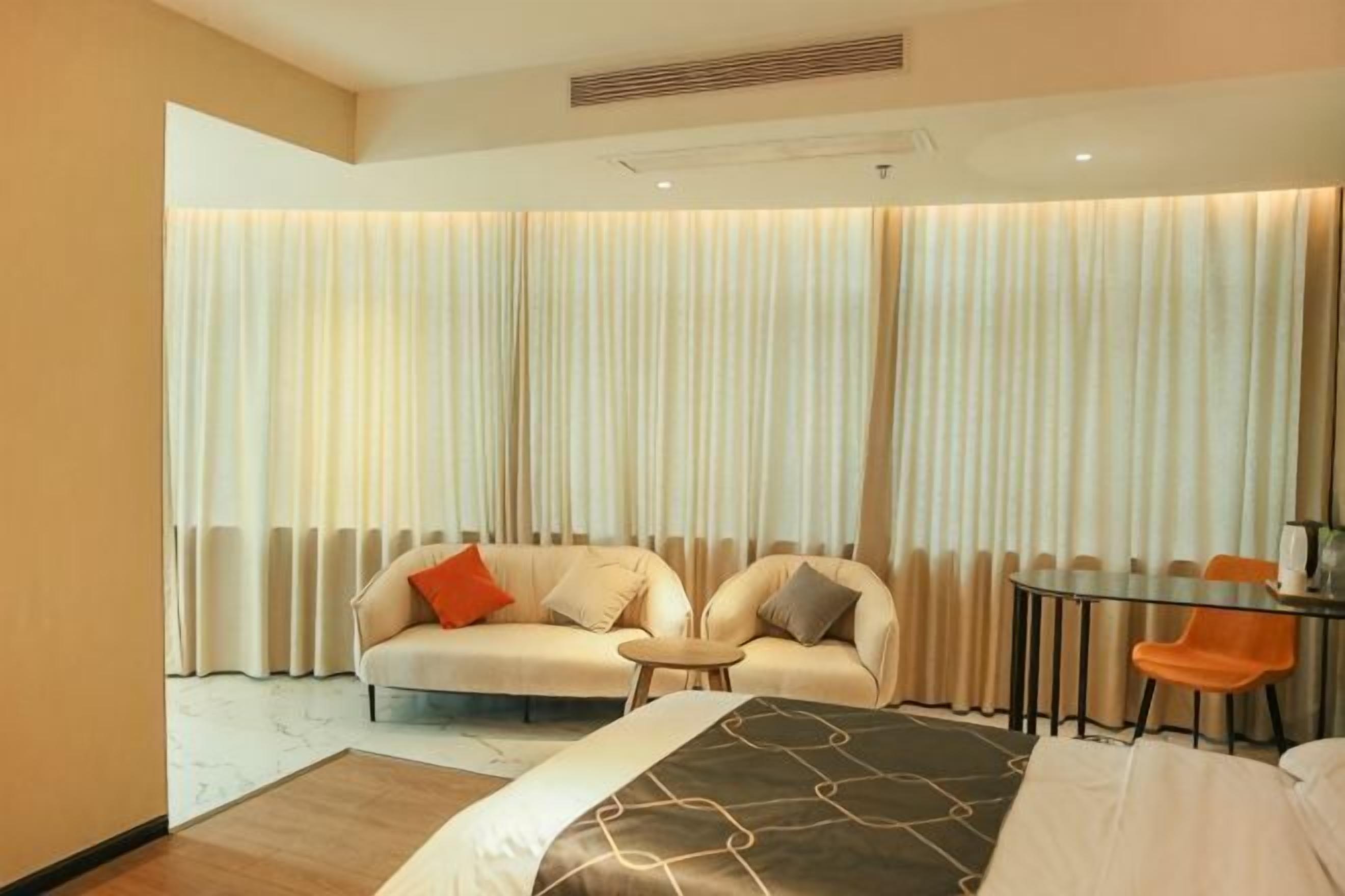 A hotel room with a bed, two sofas, a small round table, and a dining table with chairs.