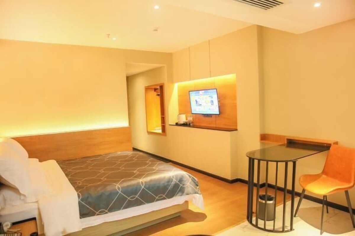 A hotel room with a bed, a desk, and a chair. There is a television mounted on the wall.