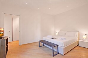 A hotel room with a bed, bedside table, lamp, and a small bench. - Les Suites Di Sara 3, Riva del Garda, Italy (Riva del Garda)