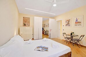 Une chambre d’hôtel avec un lit, une table à manger et des chaises, un ventilateur de plafond et des œuvres d’art accrochées aux murs.