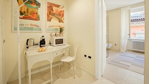 Une cuisine avec un plan de travail blanc, un four à micro-ondes, une bouilloire et une machine à café. Deux tableaux encadrés ornent le mur, ainsi qu’une chaise blanche et une porte donnant sur un balcon.