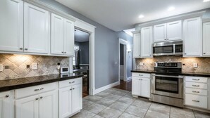 Una cocina moderna con armarios blancos, encimera negra y electrodomésticos de acero inoxidable.
