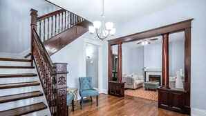 Un salón amplio con suelo de madera, una escalera de madera, un sillón azul y una chimenea.