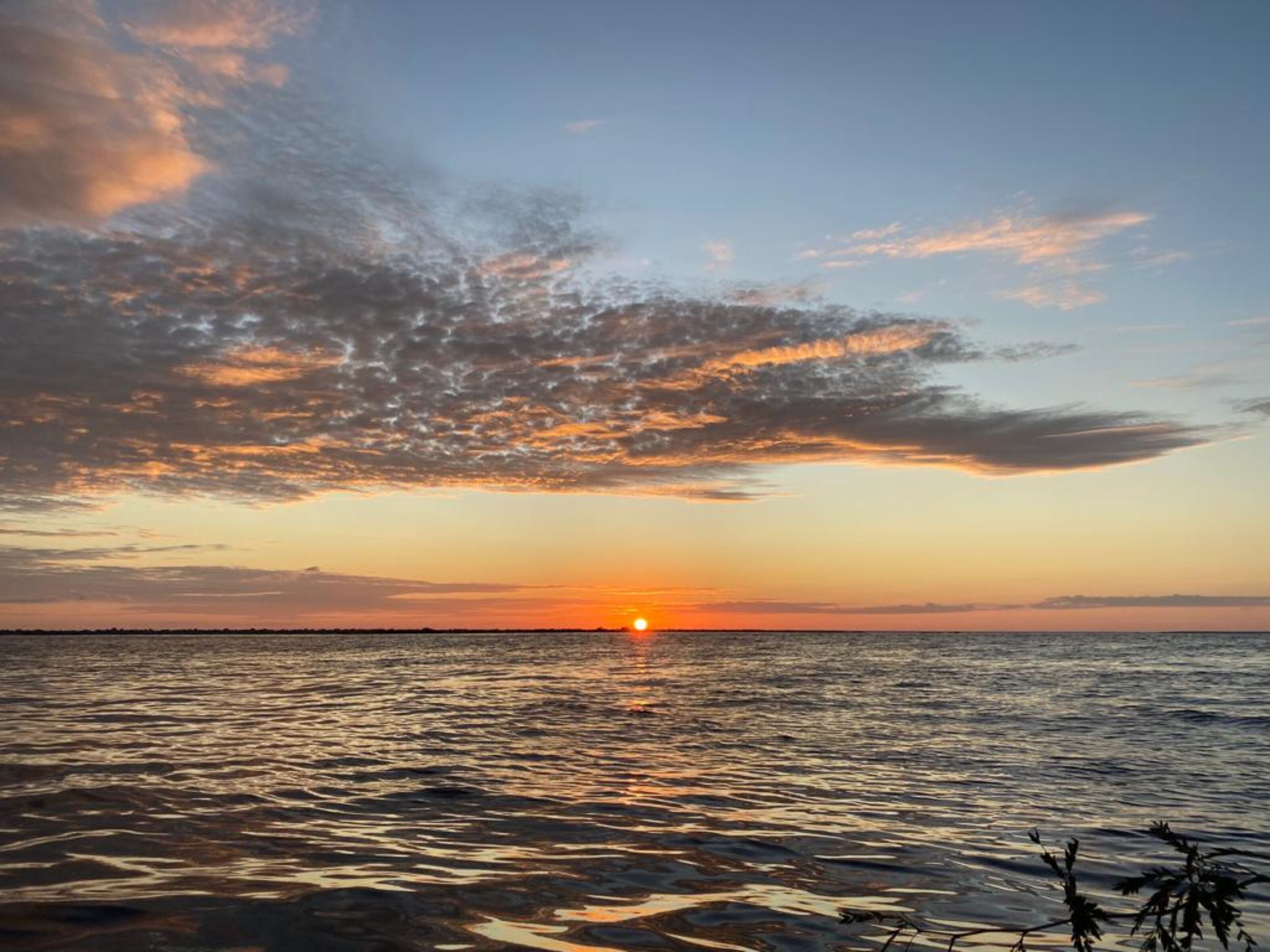 Een zonsondergang boven een rustig wateroppervlak met een verre horizon.