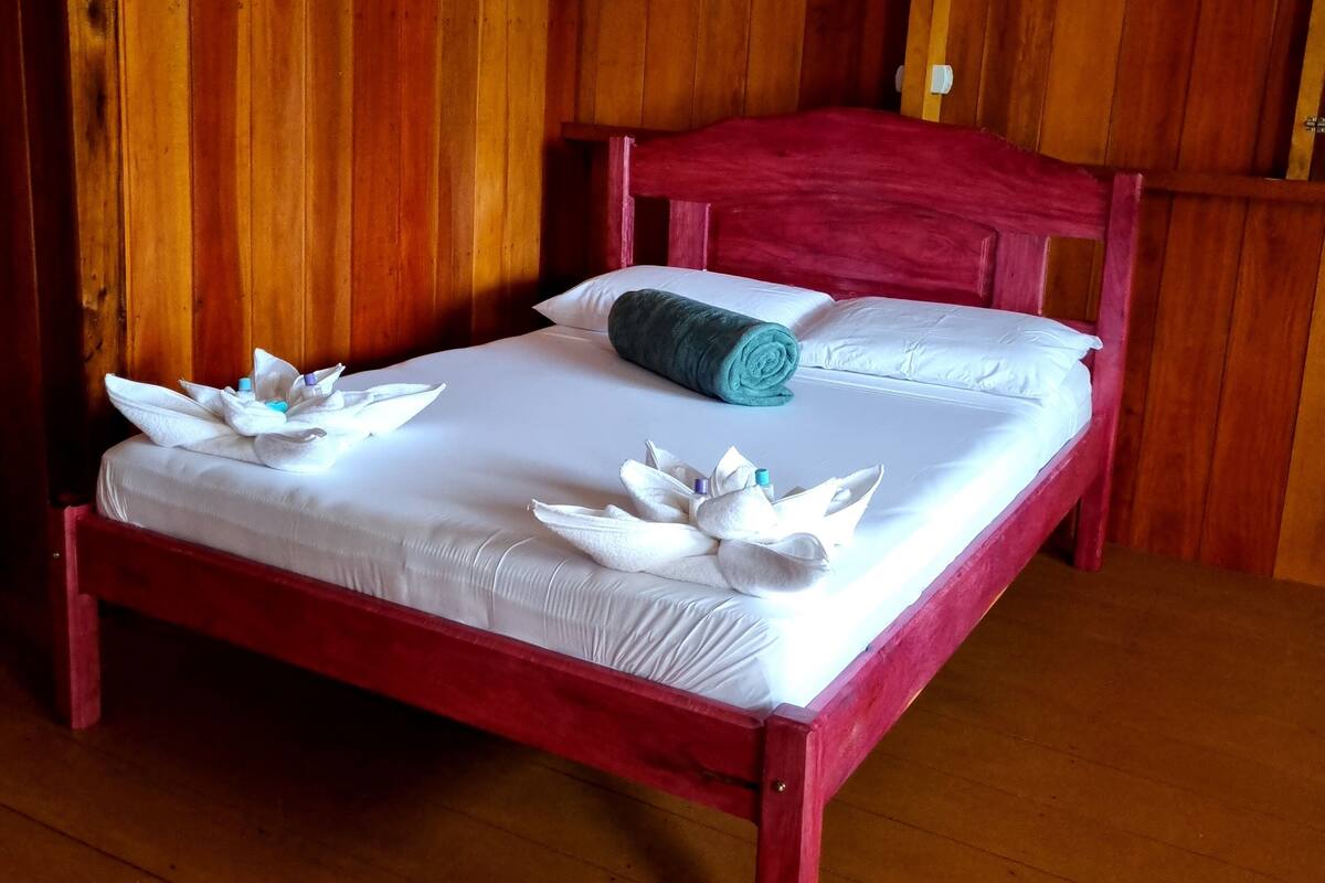 Ein hölzernes Bett mit weißen Leinen und einem roten Kopfteil in einem Zimmer mit Holzwänden.