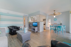 A living room with a sofa, a coffee table, a TV, and a dining area with chairs and a table. - Mid Mari - Gorgeous Nautical Condo Near Beach, Shops & Restaurants- Condo 105 (Pompano Beach)