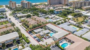 Vue aérienne d’un complexe hôtelier situé sur la côte, comprenant plusieurs bâtiments, un parking et une piscine.