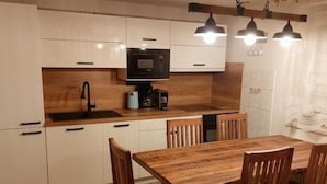 Uma cozinha moderna com armários brancos, uma mesa de jantar de madeira e luminárias pendentes.