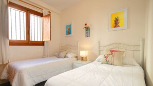 A bedroom with two single beds, a nightstand with a lamp, and a window with curtains. - Eurosol by Interhome (Calpe/Calp)