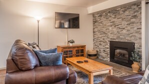 A living room with a leather sofa, a wooden coffee table, a flat-screen TV mounted on the wall, and a stone fireplace.