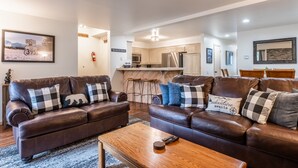 A modern living room with two brown leather sofas, a wooden coffee table, and a kitchen in the background.