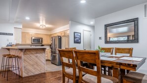 A modern kitchen with wooden cabinets, a stainless steel refrigerator, and a wooden dining table with chairs.