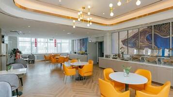 A modern dining area with round tables and chairs, a kitchen in the background, and a large window providing natural light.