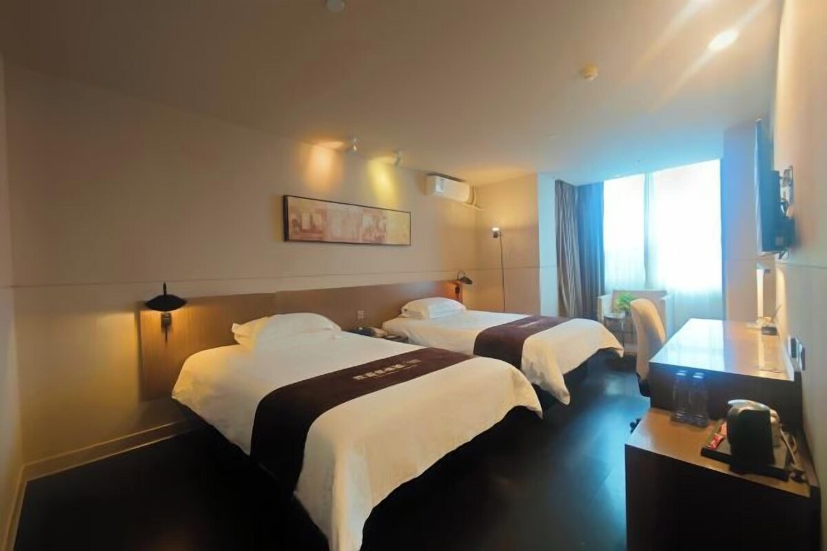 A hotel room with two beds, a desk, a chair, a TV, and a window with curtains.