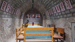 Une salle de classe aux murs de pierre, aux bancs en bois et aux affiches pédagogiques.
