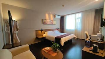 A hotel room with a bed, a desk, a chair, a coffee machine, and a small table with a plant and a tray of food.
