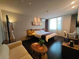A hotel room with a bed, a desk, a chair, a coffee machine, and a small table with a plant and a tray of food.