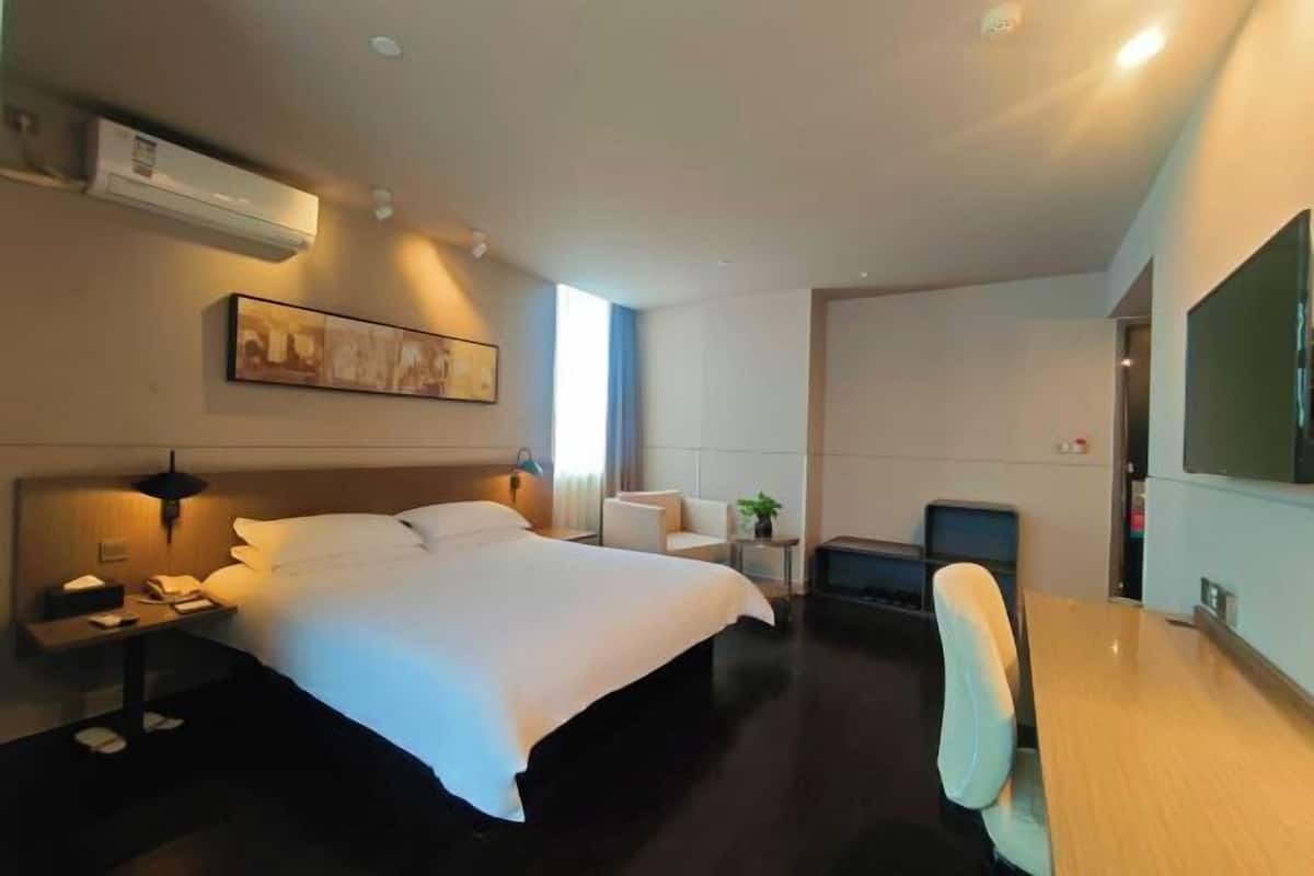 A hotel room with a large bed, a desk, a chair, a TV, and a painting on the wall.