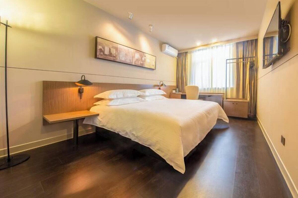 A hotel room with a large bed, bedside table, lamp, and a painting on the wall.