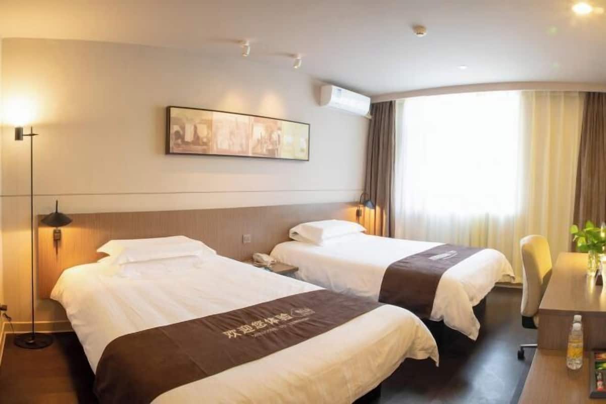 A hotel room with two beds, a desk, a chair, a lamp, and a painting on the wall.