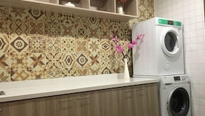 A laundry area with a washing machine and dryer, patterned tiles on the wall, and a vase with flowers on the counter. - Jinjiang Inn Select (Tianshui)