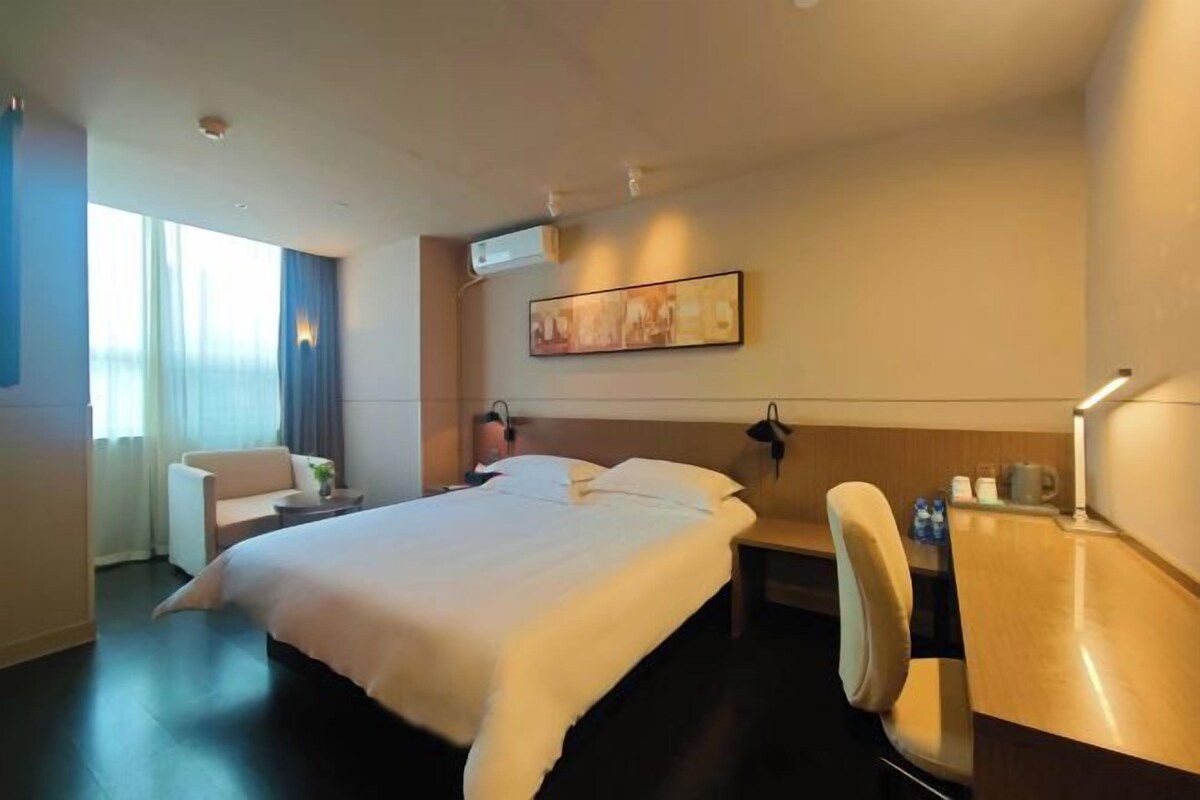 A hotel room with a large bed, a desk, a chair, and a window with curtains.