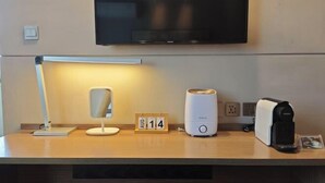 Une chambre d’hôtel équipée d’un téléviseur à écran plat fixé au mur, d’une lampe de bureau, d’une horloge numérique, d’une machine à café et d’une prise de courant.