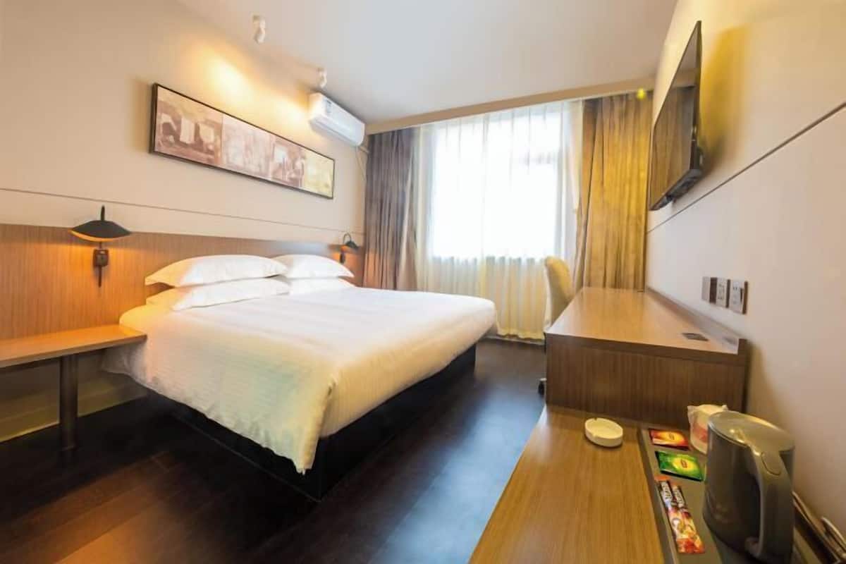 A hotel room with a bed, bedside table, desk, and a TV mounted on the wall.
