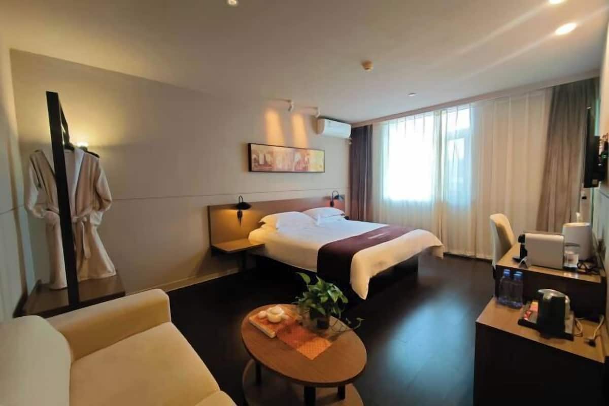 A hotel room with a bed, bedside table, chair, desk, and a small table with a plant.