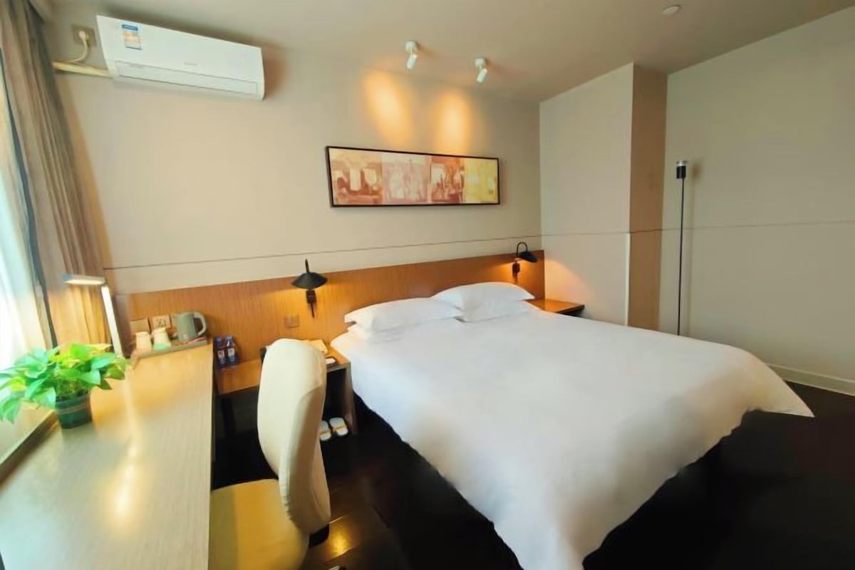Quarto de hotel com cama, mesa de cabeceira, luminária, aparelho de ar condicionado e um quadro na parede.