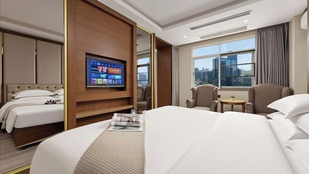 A hotel room with a bed, a TV, a seating area, and a window with a city view. - Lilai Business Hotel (Dongguan)