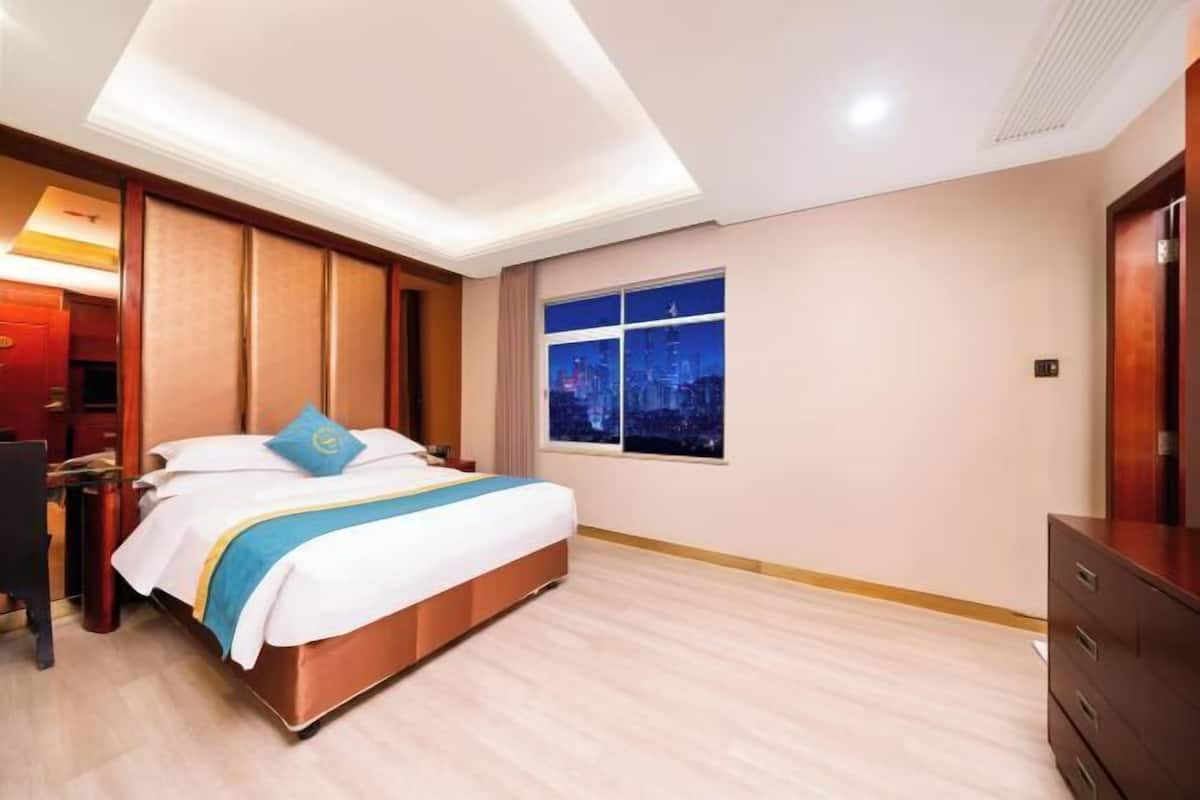 A hotel room with a bed, a night view window, a desk, and a dresser.