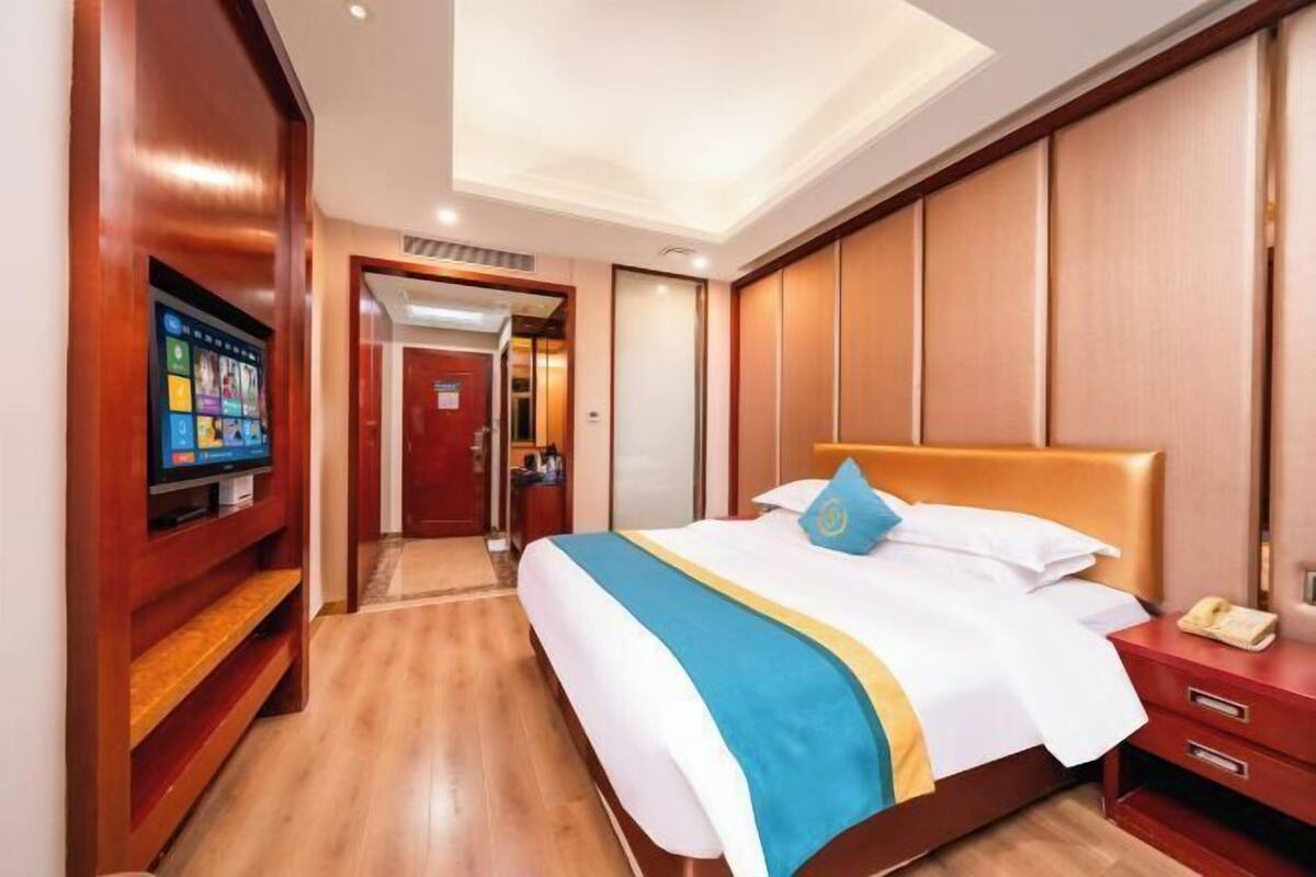 A hotel room with a bed, a TV, a wooden wardrobe, and a red door.