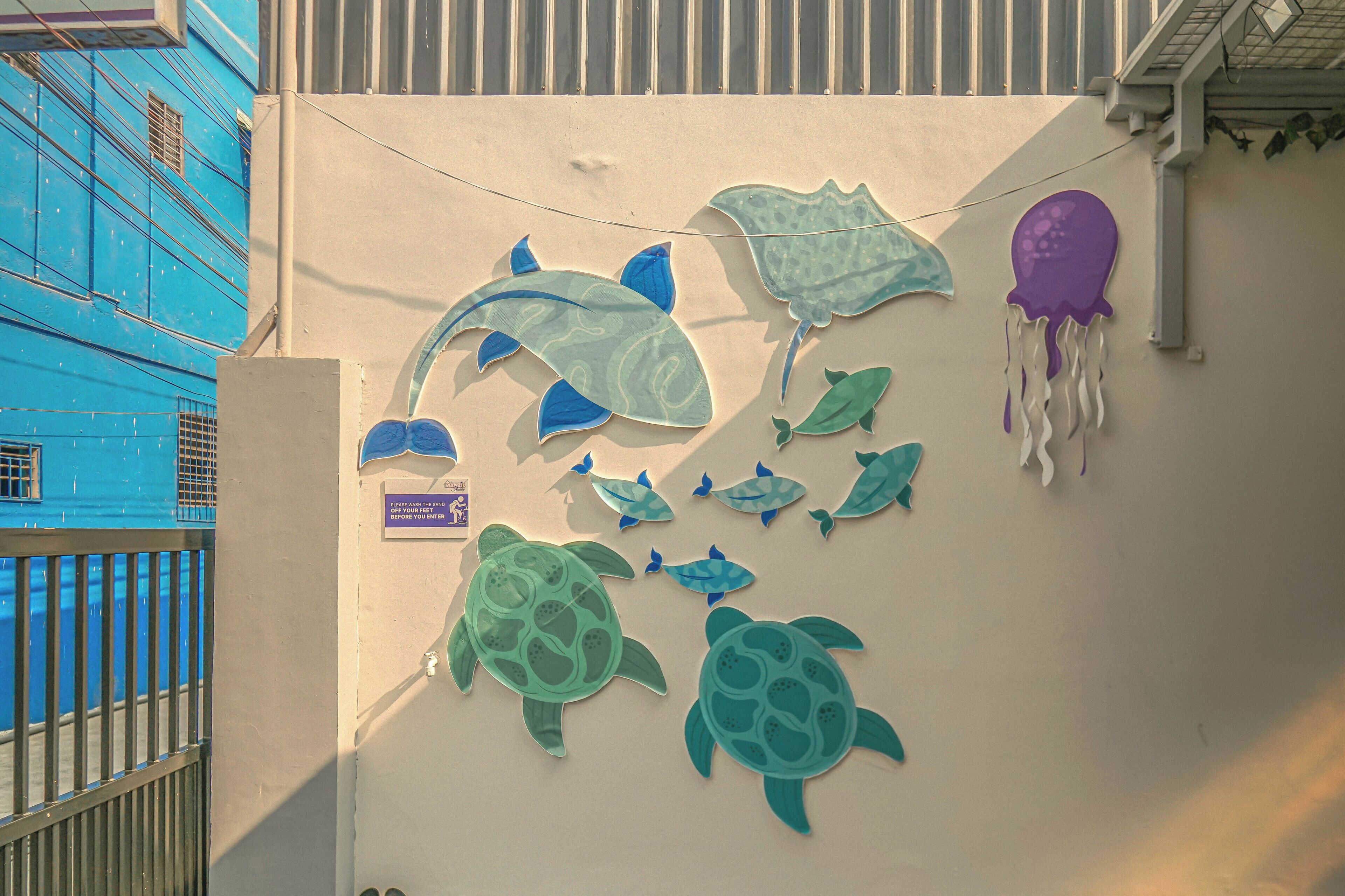 A wall with cut-out sea creatures, a sign, and a blue building in the background.