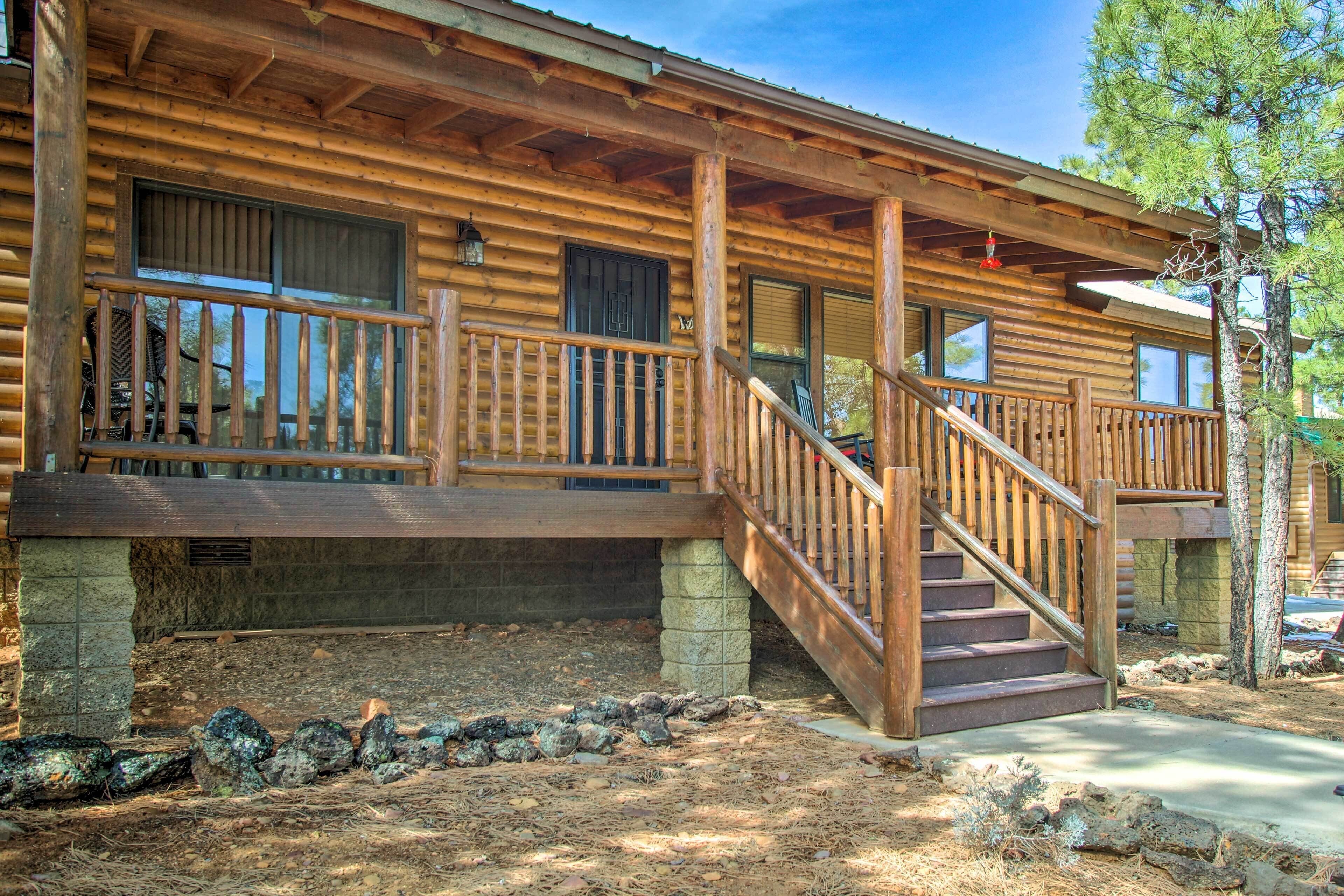 A log cabin with a wooden porch, stone foundation, and a staircase leading to the entrance.