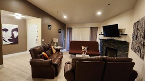 A living room with two brown leather sofas, a flat-screen TV mounted on a stone fireplace, and a large abstract painting on the wall. - ★Strip views w/amenities! Pool, fitness center, W/D in-unit & FREE parking!★ (Las Vegas)