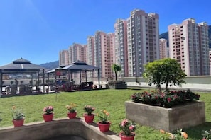 Une cour intérieure agrémentée de plantes en pot, un belvédère et, en arrière-plan, des immeubles de grande hauteur.