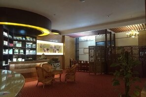 A lobby with a reception desk, wicker chairs, a red carpet, and a decorative plant.