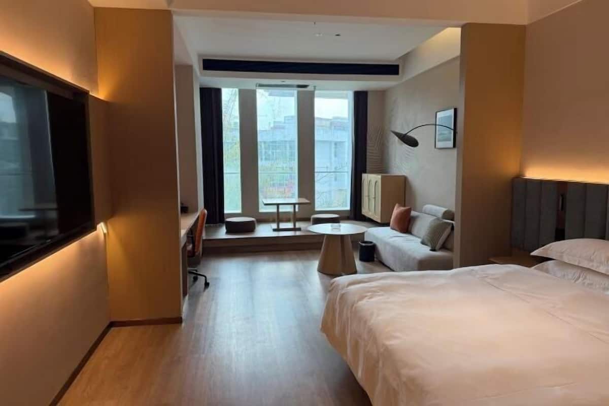 Habitación de hotel con cama, sofá, una mesita, televisor y ventana con vistas a edificios.