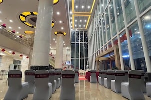 Un vestíbulo de hotel con filas de asientos, ventanas amplias y un techo alto con lámparas circulares.
