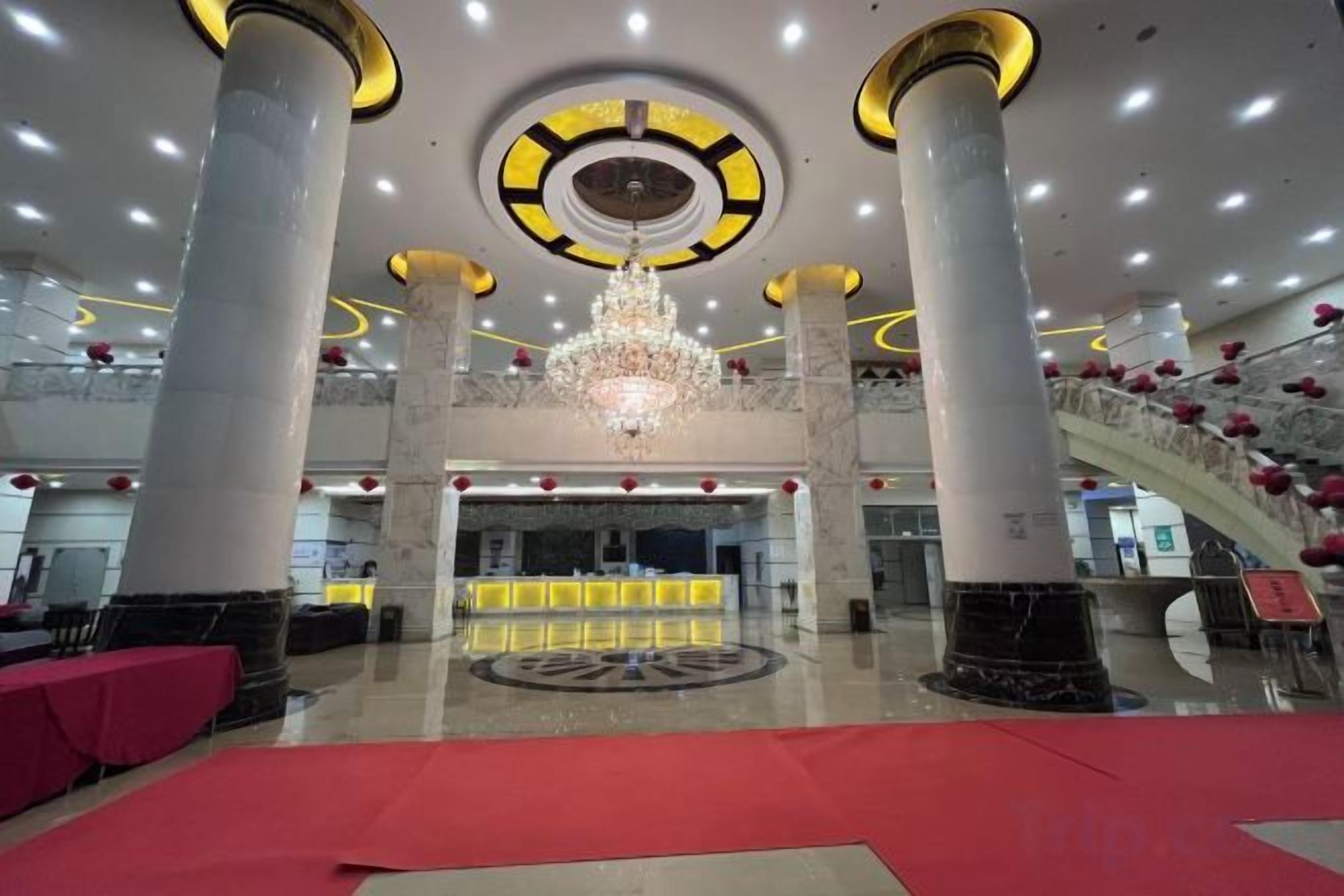 A hotel lobby with a grand chandelier, a reception desk, and a red carpet.