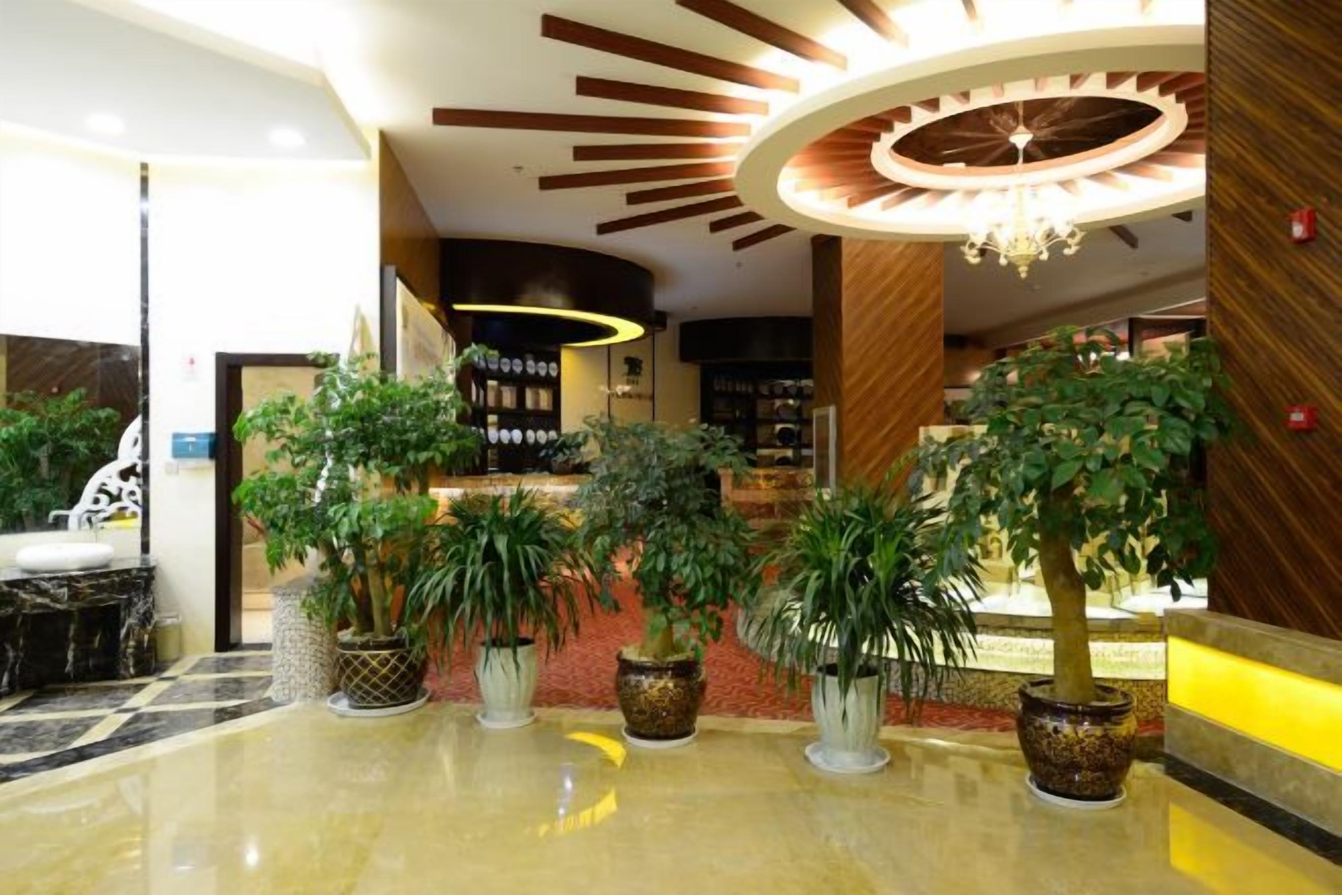 A hotel lobby with a reception desk, potted plants, and a chandelier.