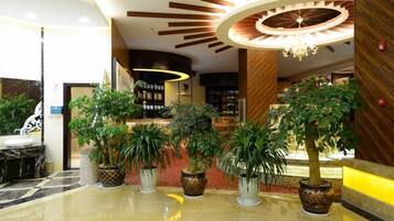 A hotel lobby with a reception desk, potted plants, and a chandelier.