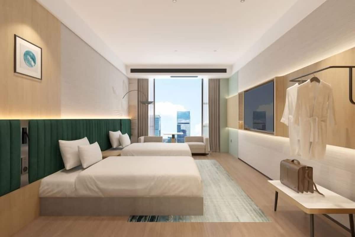 Habitación de hotel con dos camas, zona de estar, vistas a la ciudad y perchero.