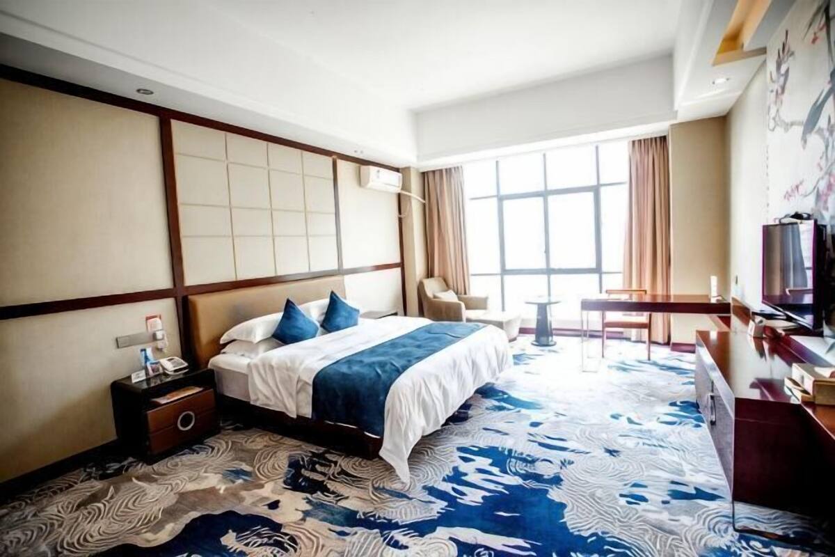 Una habitación de hotel con una cama grande, un escritorio, una silla, un televisor y una ventana.