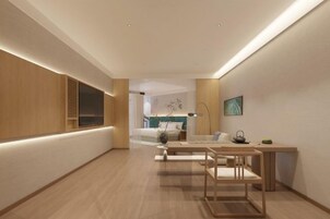 Una habitación de hotel moderna con suelo de madera, una cama con ropa blanca, un escritorio con lámpara y un cuadro en la pared.