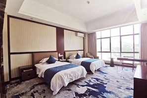 A hotel room with two beds, a large window, a desk, and a patterned carpet.